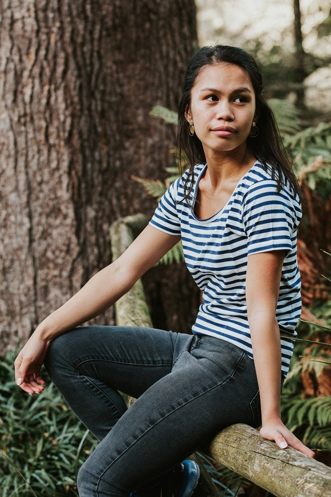 Female model outside sitting on tree branch wearing Pūkeko Bellbird Tee - White Navy Stripe