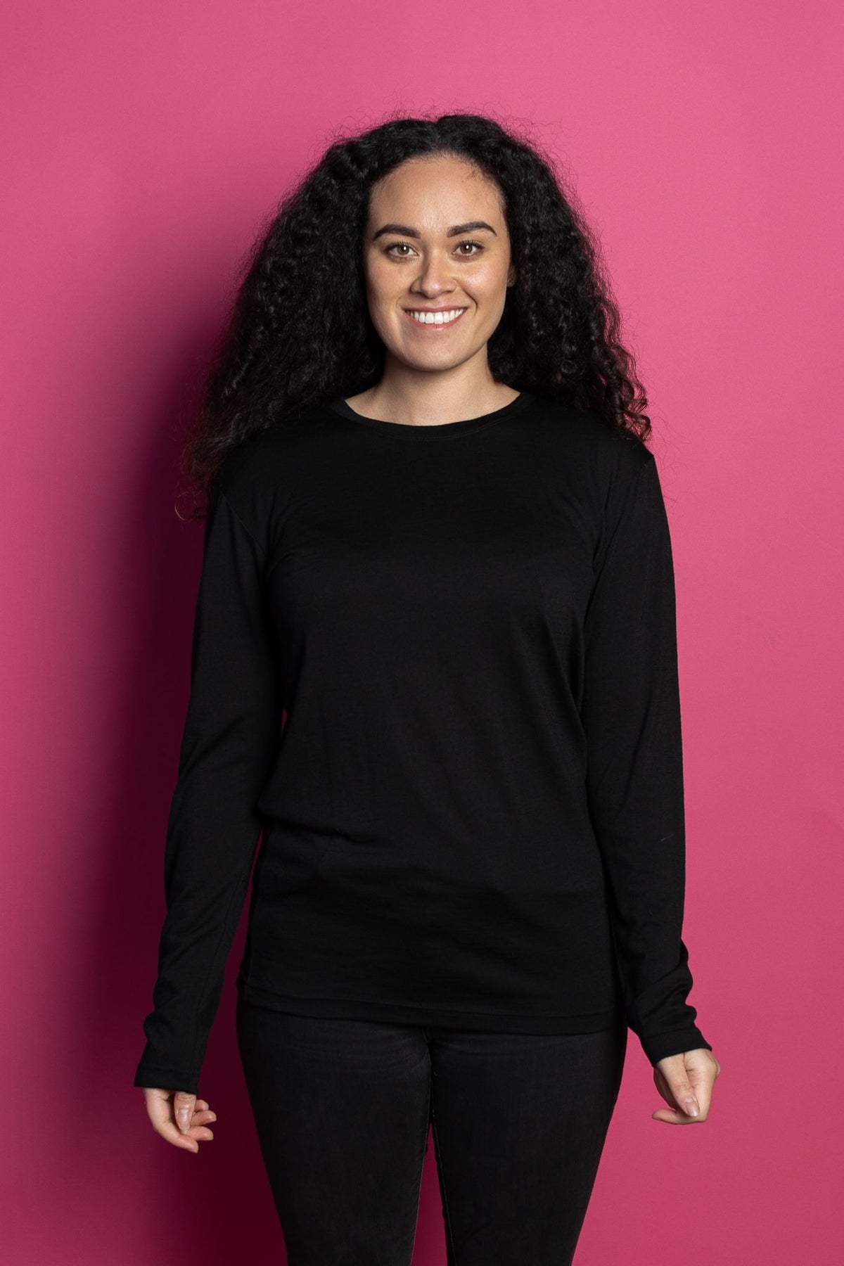 Female model wearing black marvel merino long sleeve tee against pink background