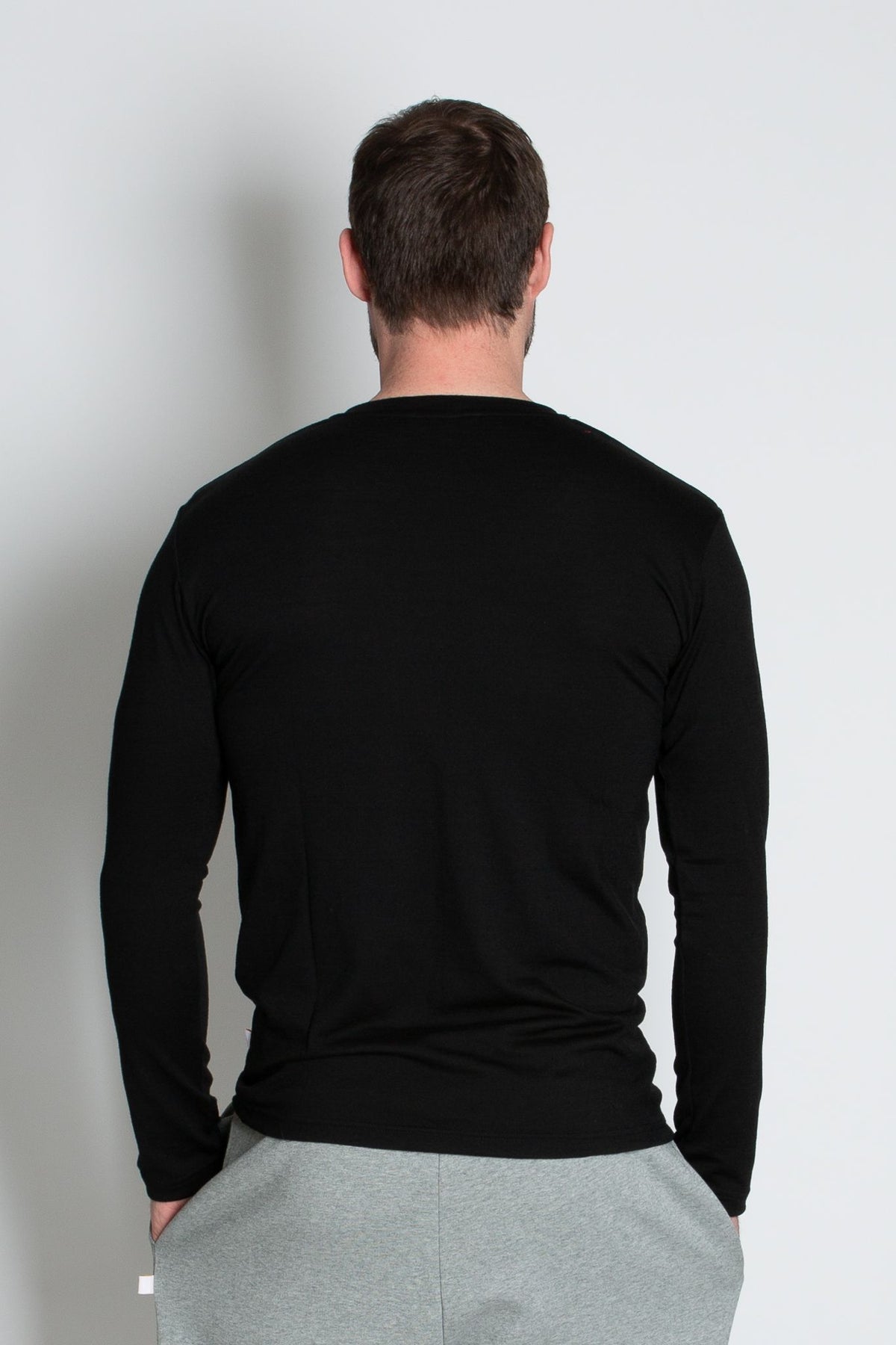 Back view of male model wearing black marvel merino long sleeve tee against blue background