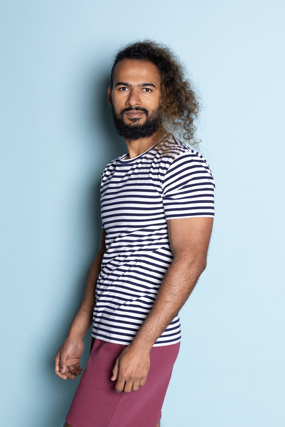 Man wearing pukeko stripe tui tee and burgundy lounge pants in front of a blue background